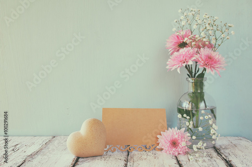 fresh white and pink flowers, heart next to vintage empty card over wooden table
