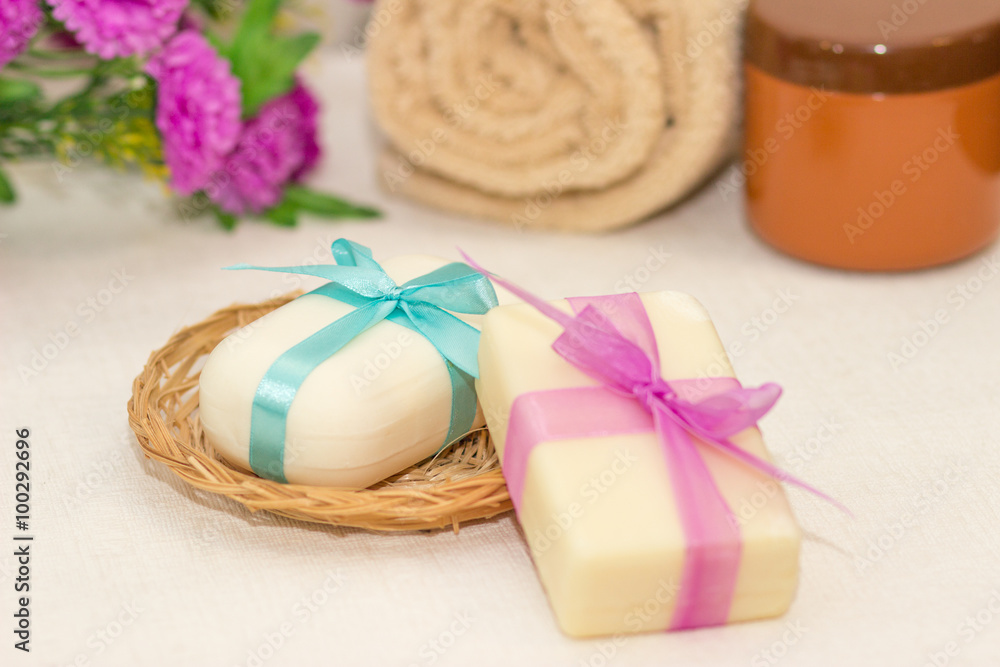 Two pieces of soap with a basket with a bows , flowers , towel a