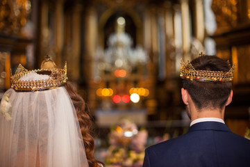 Fairytale couple, bride and groom in crowns during wedding ceremony in church