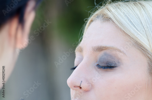 Professional makeup artist applying make up on a beautiful young blonde model face for a photoshoot