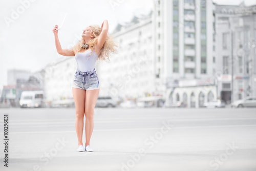 Music and selfie / Happy young woman with vintage music headphones around her neck, taking selfie with tablet pc and smiling happily against urban city background. © Fisher Photostudio