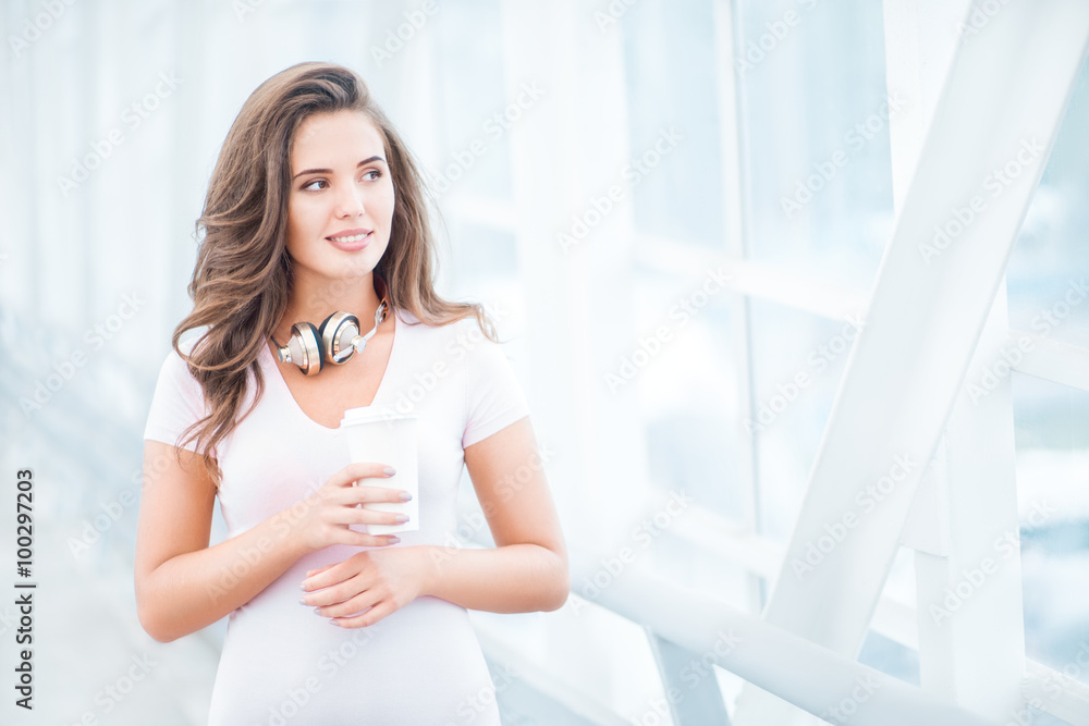 Peaceful morning / Happy young woman wearing music headphones, standing on the bridge with a take away coffee cup and looking aside against urban background. Peaceful morning / Happy young woman wearing music headphones, standing on the bridge with a take away coffee cup and looking aside against urban background.