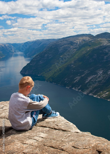 Norway. The thought boy sits on the edge of the rock