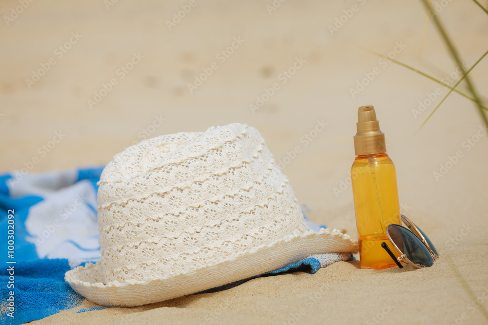 Beach set hat and sunscreen lotion lying on sand Beach set hat and sunscreen lotion lying on sand