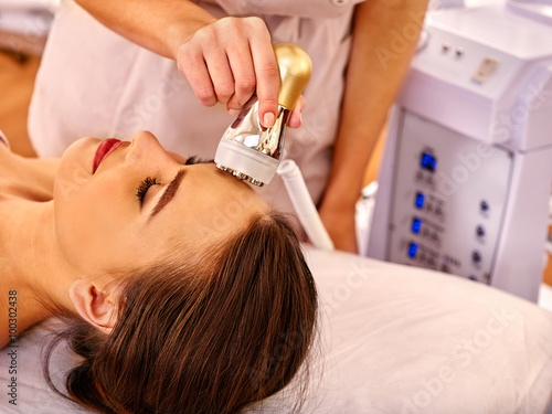 Young happy woman receiving electroporation  facial gold therapy at beauty salon.  photo