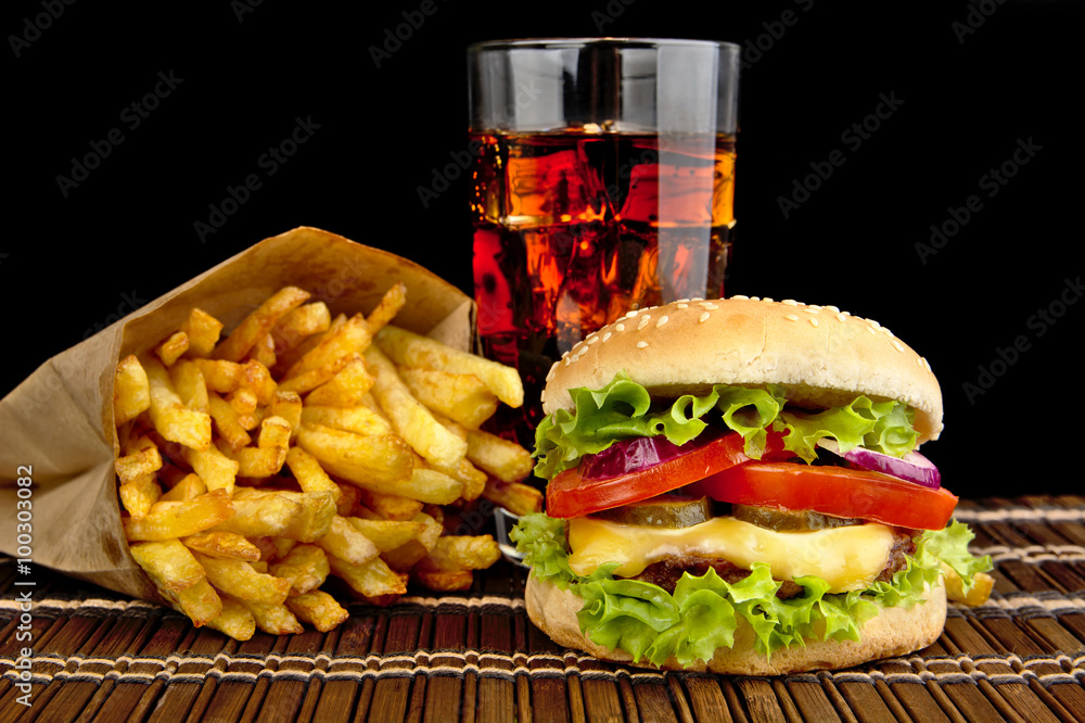 Φωτογραφία Cheeseburger with french fries with glass of cola on wooden mat on black