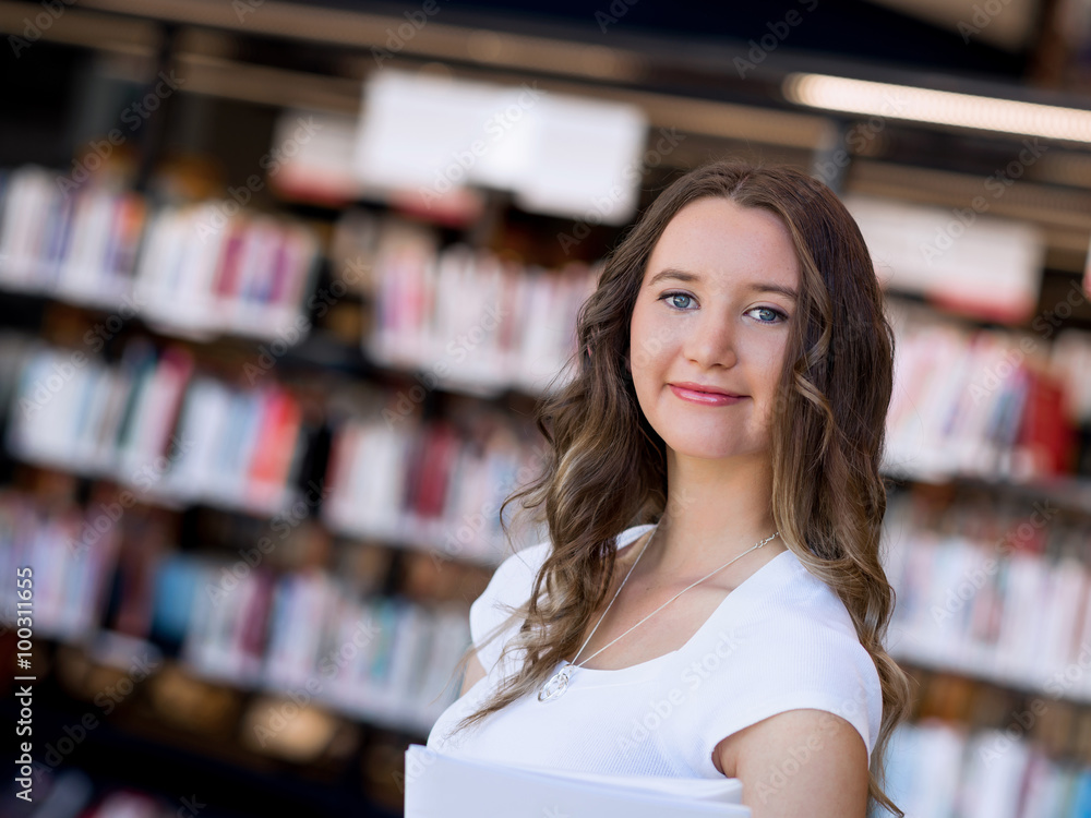 Happy female student holding books at the library Happy female student holding books at the library