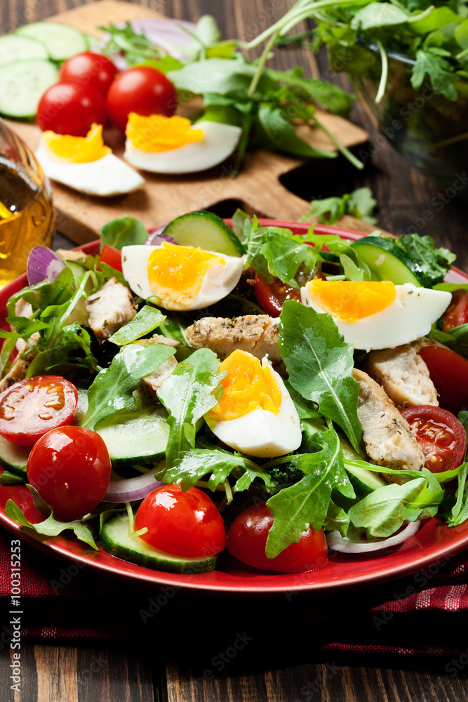 Fresh salad with chicken, tomatoes, eggs and arugula on plate