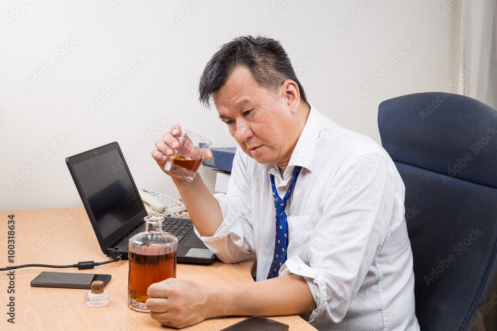 Frustrated and stressful Asian manager drinking hard liquor in office Frustrated and stressful Asian manager drinking hard liquor in office