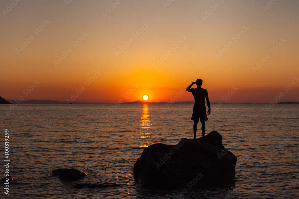 A man standing on the shore watching the sunset