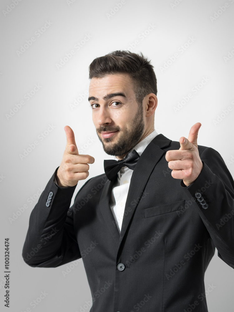 Young cheerful bearded man pointing finger gun gesture at camera. Desaturated portrait over gray studio background with retro vignette. Young cheerful bearded man pointing finger gun gesture at camera. Desaturated portrait over gray studio background with retro vignette.