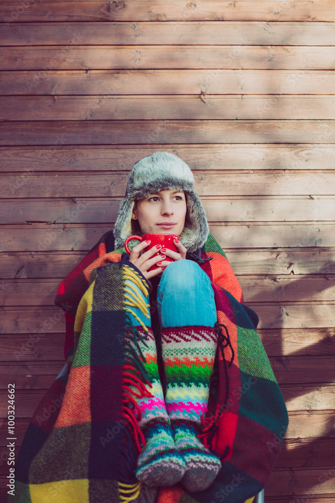 Young woman resting outdoor, drinking coffee or tea under a warm blanket