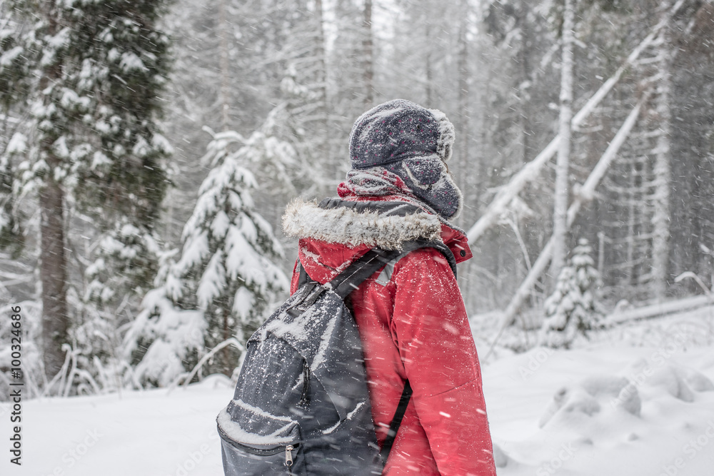 Fototapeta premium Woman winter hiking. Beautiful young woman enjoying the falling snow dressed in a winter scarf and cap and with a satchel on her back with copyspace.