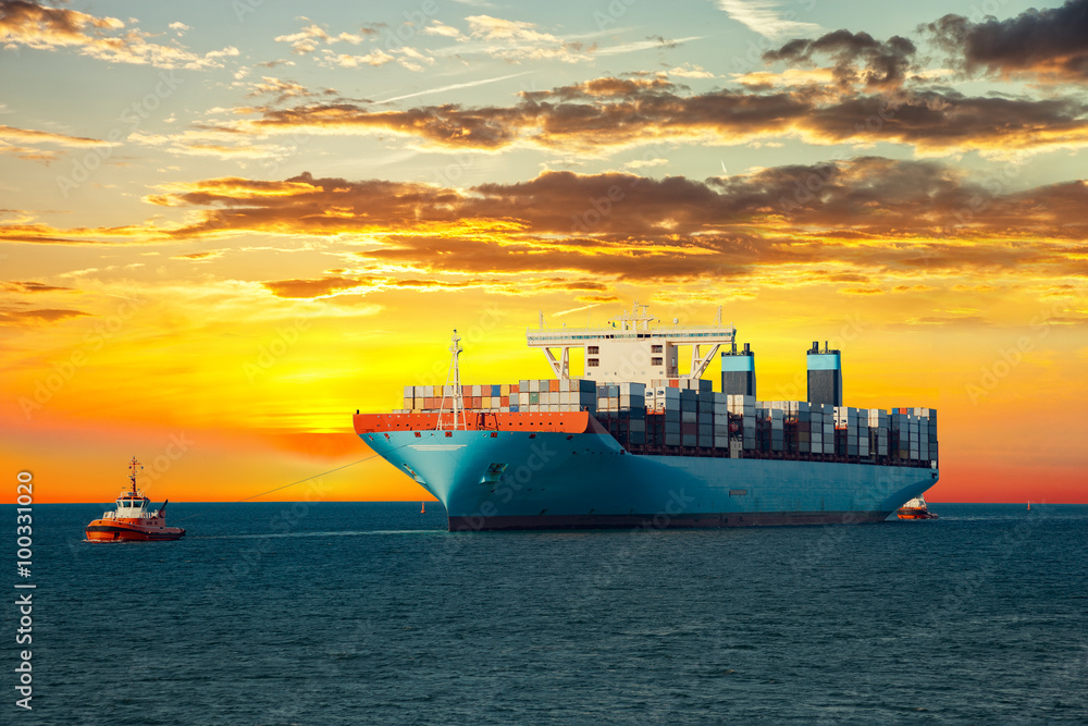 Tugboats assisting container ship on sea in the morning.