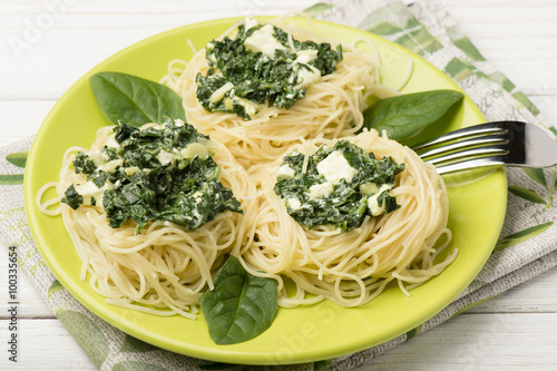 Italian pasta with spinach and feta on green plate on the wooden background.