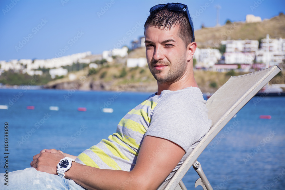 nadsome young man enjoying the summer holiday relaxing on a sunbed on a sea background