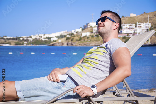 nadsome young man enjoying the summer holiday relaxing on a sunbed on a sea background © boryanam