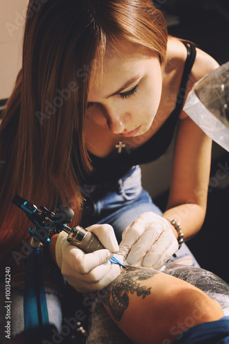Woman tattoo master in a process of creation tattoo with a crown on a man`s hand.