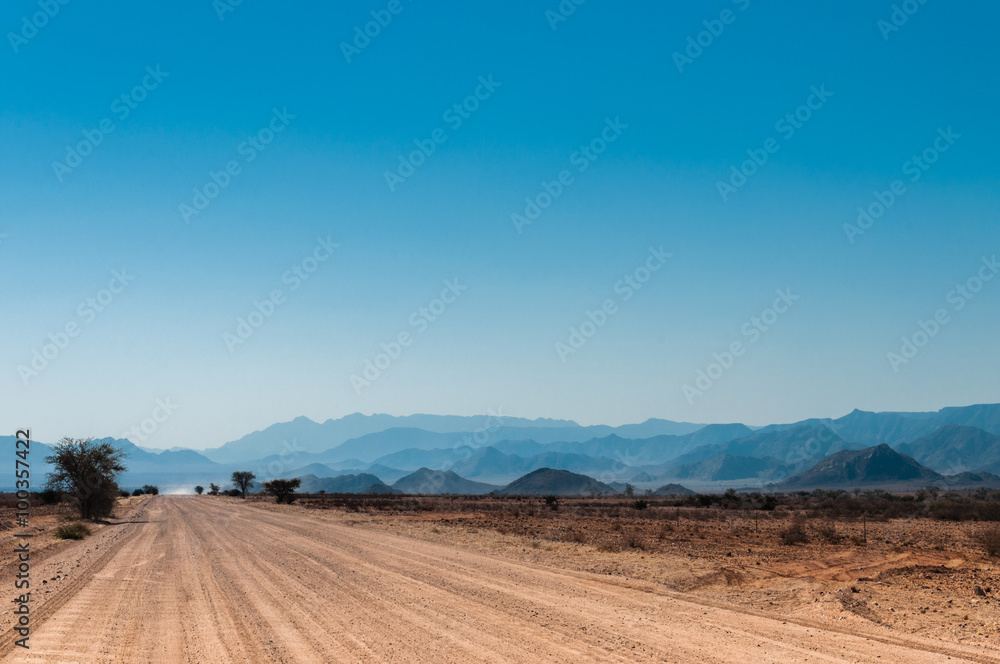 Schotterpiste in der Namibwüste mit Naukluftgebirge als Silhouette; Namibia