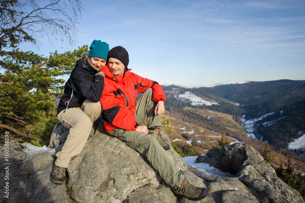 Young couple of hikers sitting on top of mountain. Smiling and l