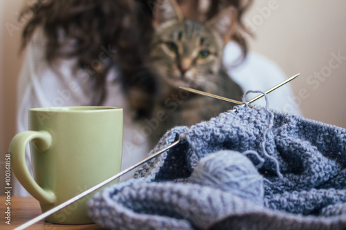 On the table is a knitting and a cup, in the background a girl a