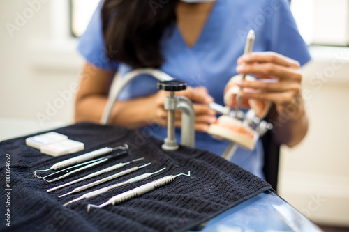 Closeup portrait, young oral professional student practicing dental procedures on plastic teeth, wax typodont mounted on table. Drilling cavity preparations and filling with restorative materials