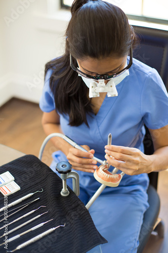 Closeup portrait, young oral professional student practicing dental procedures on plastic teeth, wax typodont mounted on table. Drilling cavity preparations and filling with restorative materials