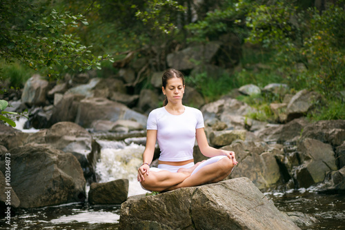 Beautiful young woman meditating in yoga pose at a mountain stream. 