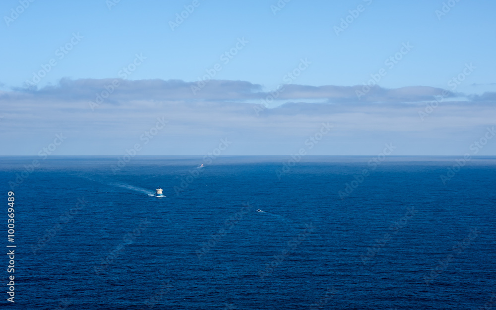 Three boats in distance on blue ocean under forming clouds