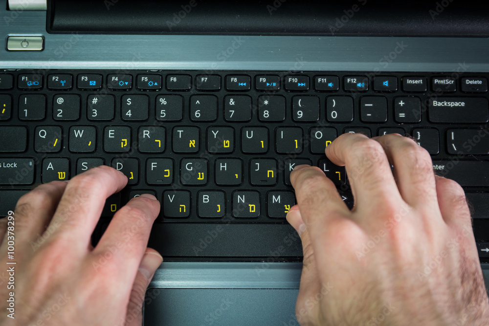 Man typing on a keyboard with letters in Hebrew and English - Laptop keyboard - Top View - Dark atmosphere Man typing on a keyboard with letters in Hebrew and English - Laptop keyboard - Top View - Dark atmosphere