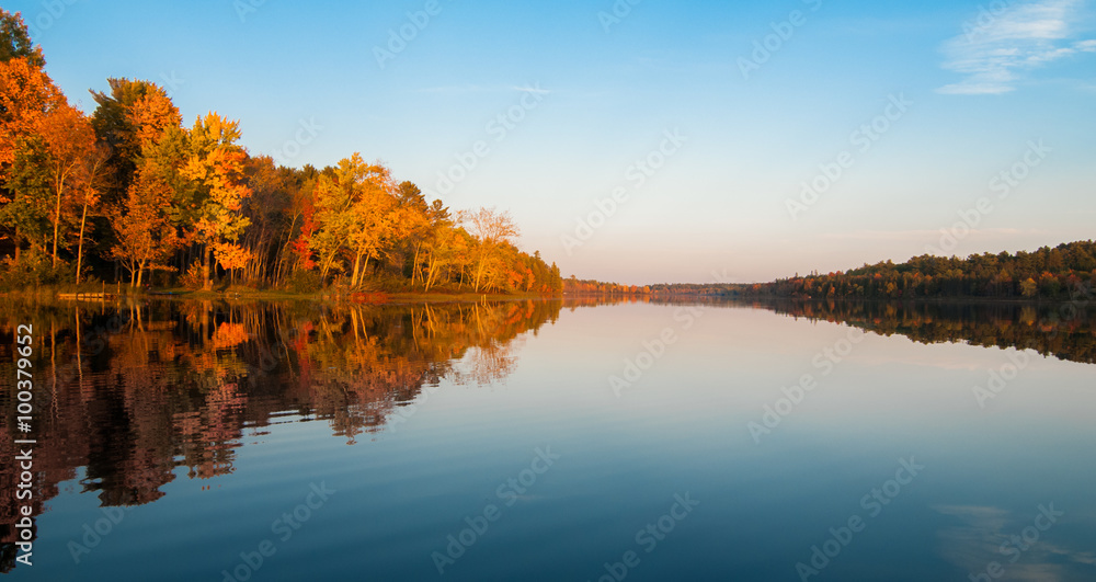 Northern Ontario lake at sundown on a late summer's day. Mirror-like reflections and glowing orange forest. Northern Ontario lake at sundown on a late summer's day. Mirror-like reflections and glowing orange forest.