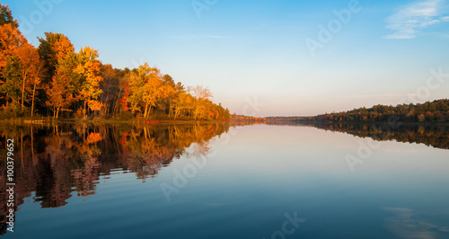 Northern Ontario lake at sundown on a late summer's day.  Mirror-like reflections and glowing orange forest.