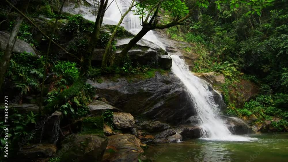 Tracking shot of a jungle waterfall cascading down into a dark green pool. Tracking shot of a jungle waterfall cascading down into a dark green pool.