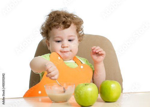 little child eats with spoon sitting at table with fruits 