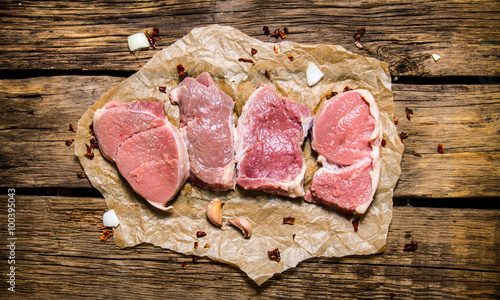 Steaks from raw meat with spices. On wooden background.