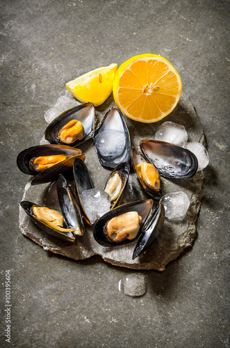 Fresh clams with lemon and ice on a stone stand.