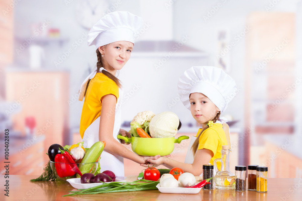 two little chefs in the kitchen holding a pan with vegetables two little chefs in the kitchen holding a pan with vegetables