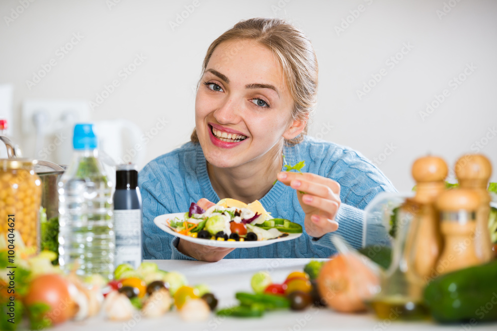 Smiling girl in blue sweater decorating salad on plate