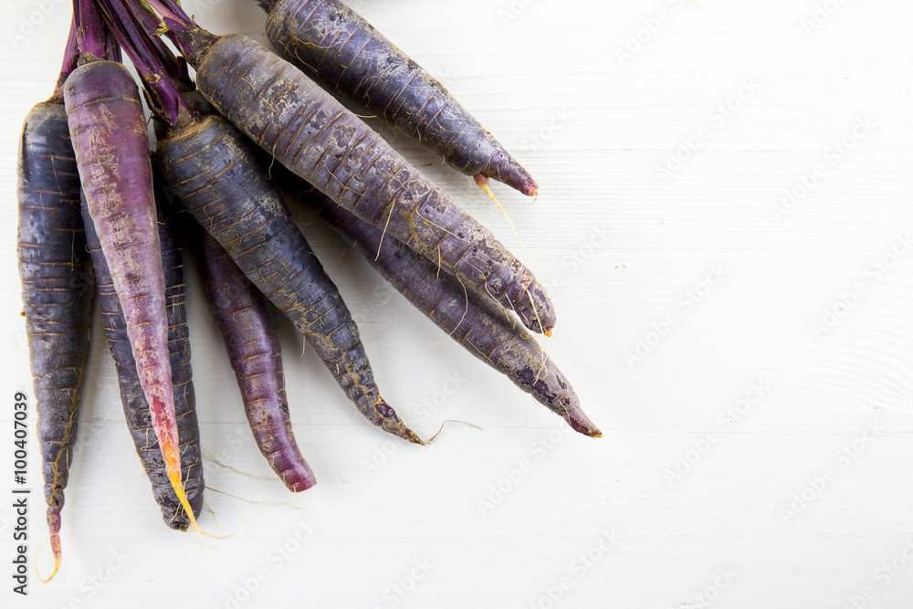 Bunch of heirloom purple carrots, over white and wooden backgrou Bunch of heirloom purple carrots, over white and wooden backgrou