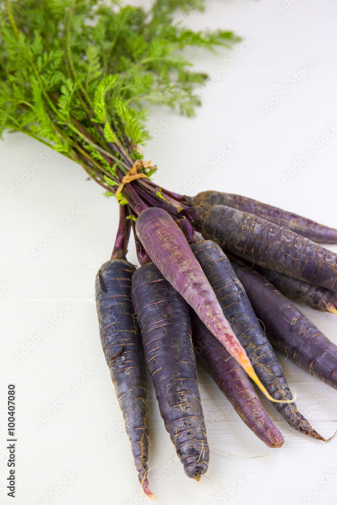 Bunch of heirloom purple carrots, over white and wooden backgrou Bunch of heirloom purple carrots, over white and wooden backgrou