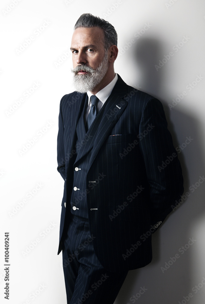 Portrait of bearded businessman wearing trendy suit and stands against the empty white wall. Vertical Portrait of bearded businessman wearing trendy suit and stands against the empty white wall. Vertical