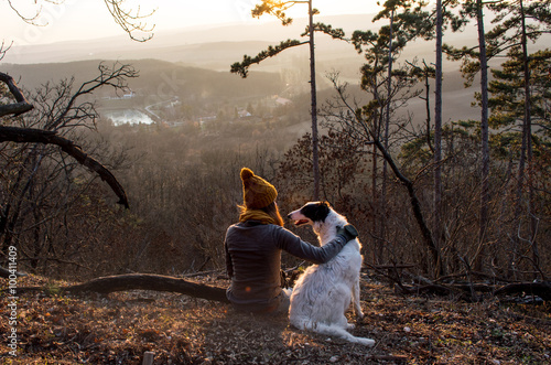 Girl sitting with dog in forest with beautiful view