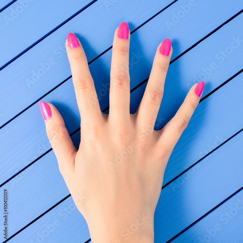Photo Female hand with pink nails on blue wooden background