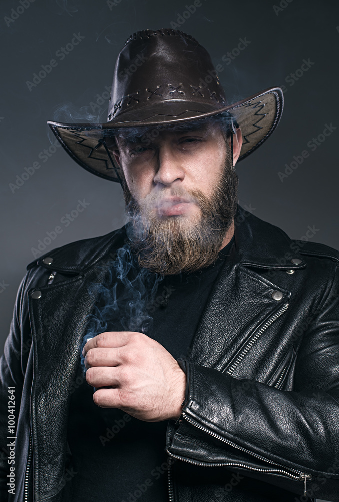Smoking man with a beard and mustache wearing a cowboy hat. Smoking man with a beard and mustache wearing a cowboy hat.