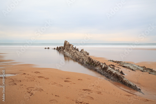 Sopelana beach with an elongated rock in the foreground on a cloudy day, in Sopelana, Spain