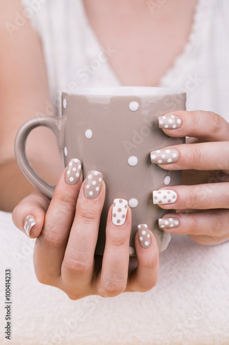 Beauty treatment photo of nice manicured woman fingernails holding a cup.
