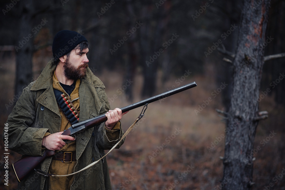 Naklejka premium brutal hunter, bearded man in warm hat with a gun in his hand