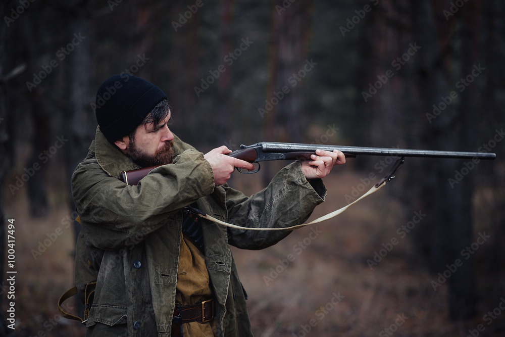 Fototapeta premium brutal hunter, bearded man in warm hat with a gun in his hand