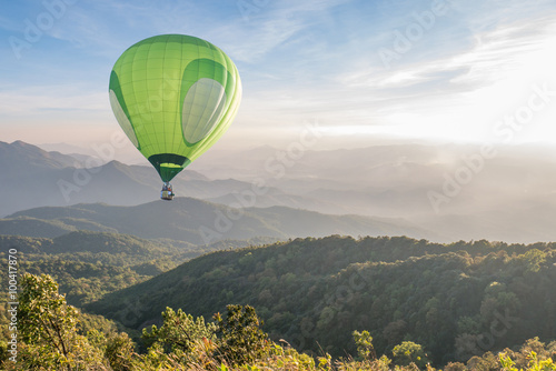 Green hot air balloon over high mountain landscape at sunset