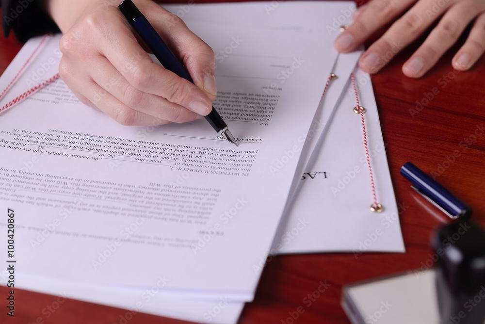 Closeup of a hand signing a last will by a pen.